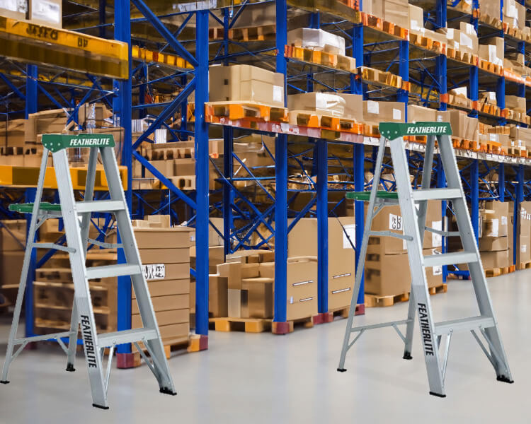 Featherlite step ladders positioned in a large warehouse with extensive shelving units.