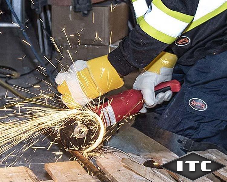 A worker wearing protective gear uses an angle grinder on a metal bar, causing sparks to fly in a workshop.