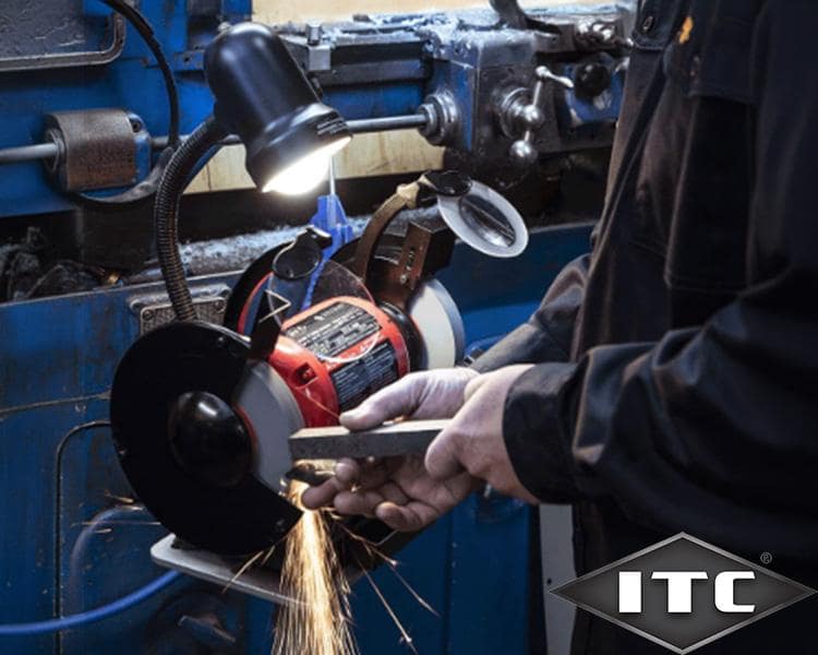 A set of wrenches organized on a red holder laid on a wooden table, with a box of various tools slightly blurred in the background, displaying the itc logo.