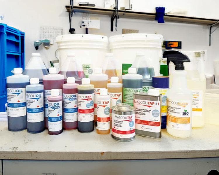 Colorful chemical containers and bottles labeled in French, arranged on a lab countertop, suggesting a chemical or cleaning product laboratory setup.