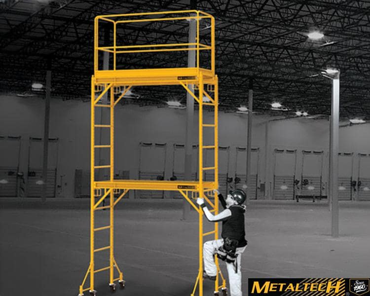 A Metaltech worker stands on a ladder inside an industrial building, surrounded by metal structures and machinery.