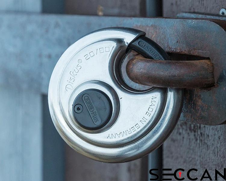 ABUS circular discus padlock secured in a metal latch, with visible weathering and rust, showcasing the Seccan brand name on textured wood.