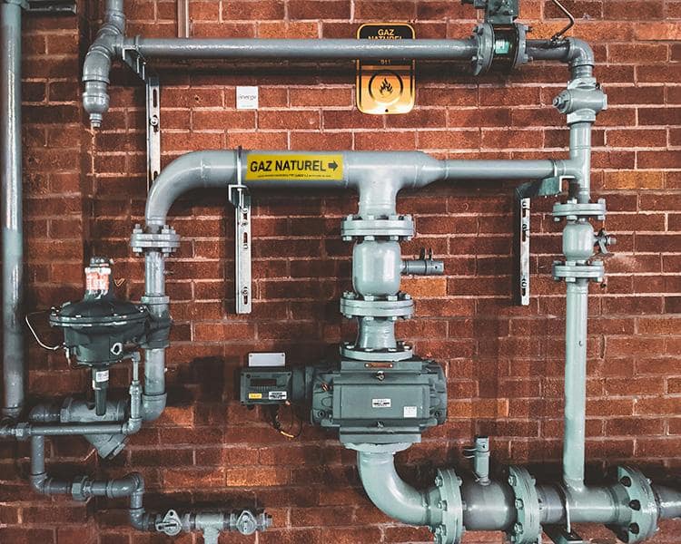 An arrangement of metallic pipes and valves affixed to a rustic brick wall, highlighting industrial design elements.