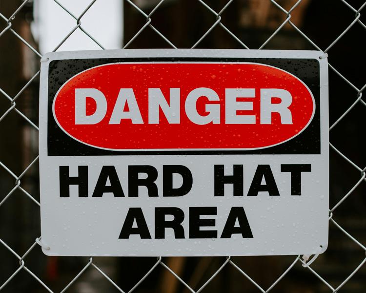 A caution sign displayed on a chain link fence, alerting individuals to nearby hazards.