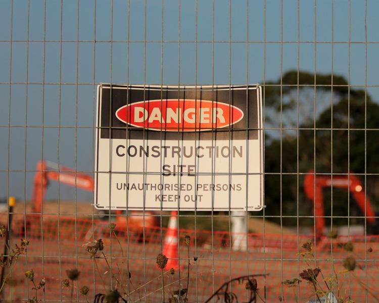 A warning sign attached to a chain link fence, indicating potential danger in the surrounding area.